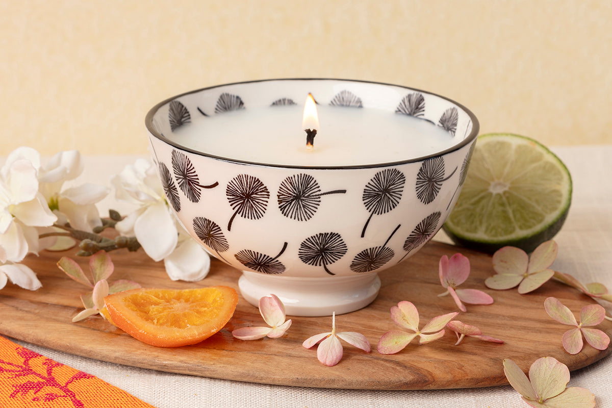 Candle in a decorative bowl with flowers and fruit on a wooden board