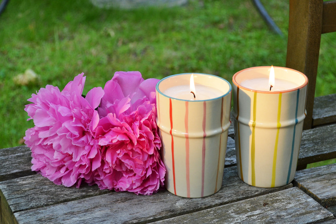 Two striped candles on a wooden surface with pink flowers in the background.
